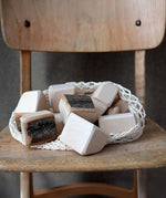 Grimm's 15 wooden blocks with natural bark in a net storage bag placed on a wooden chair.