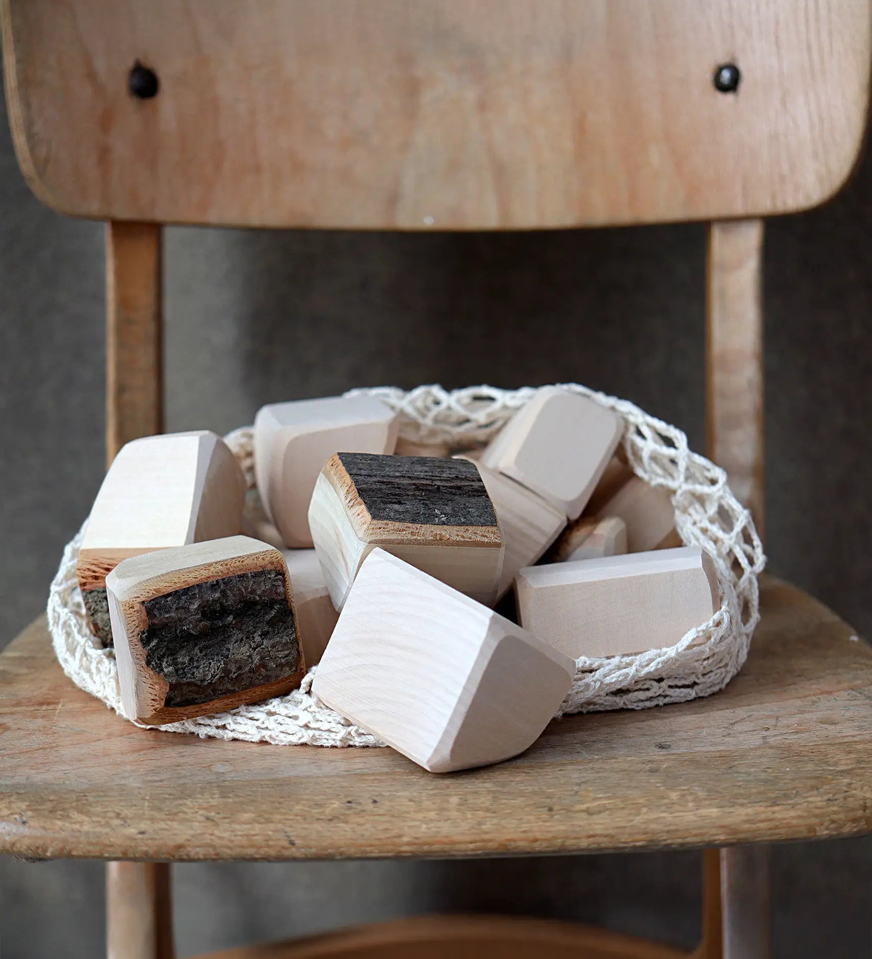 Grimm's 15 wooden blocks with natural bark in a net storage bag placed on a wooden chair.