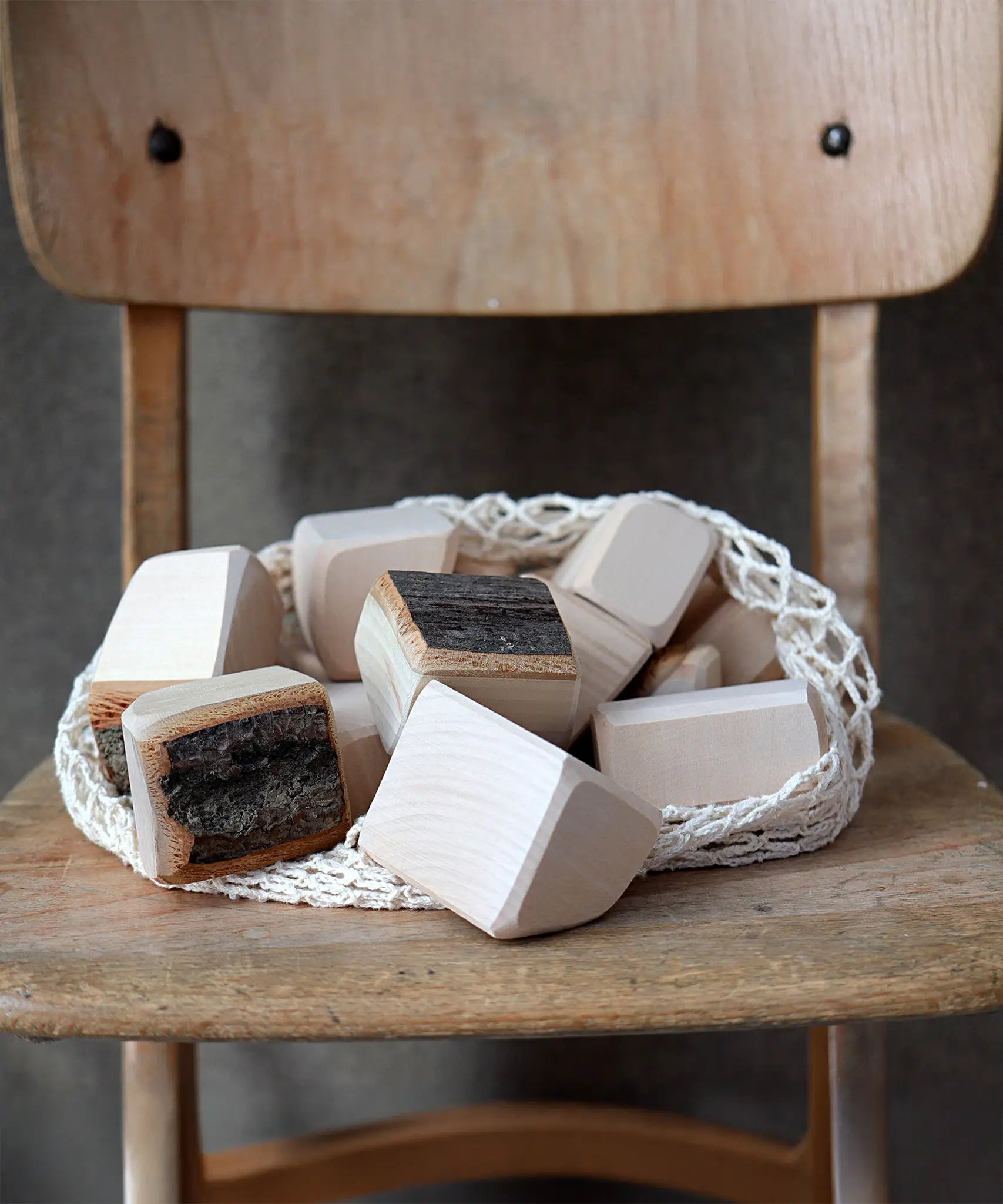 Grimm's 15 wooden blocks with natural bark in a net storage bag placed on a wooden chair.