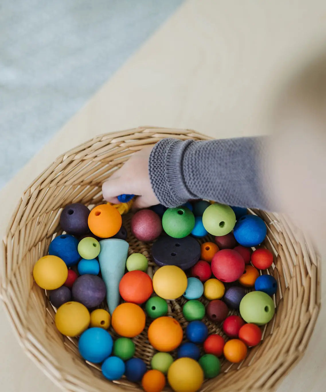 A mix of 20 and 12mm Grimms beads in a basket with small child's hand reaching in showing scale