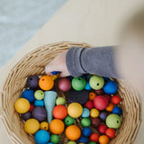 A mix of 20 and 12mm Grimms beads in a basket with small child's hand reaching in showing scale