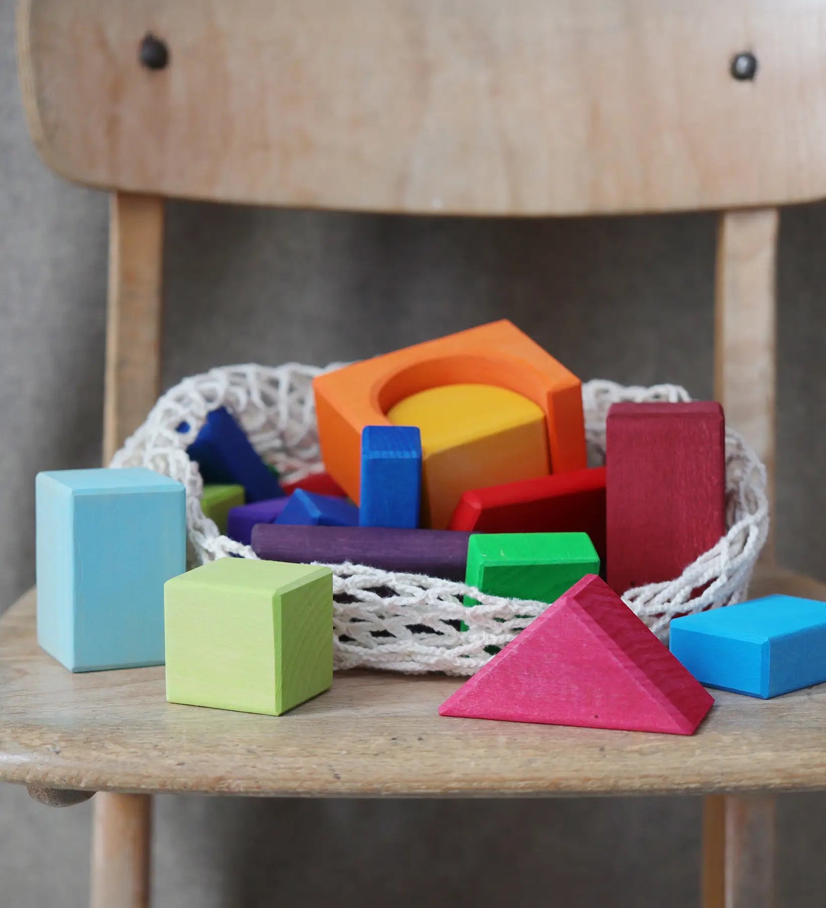 Grimm's 30 Coloured wooden Geo Blocks placed on a wooden chair.