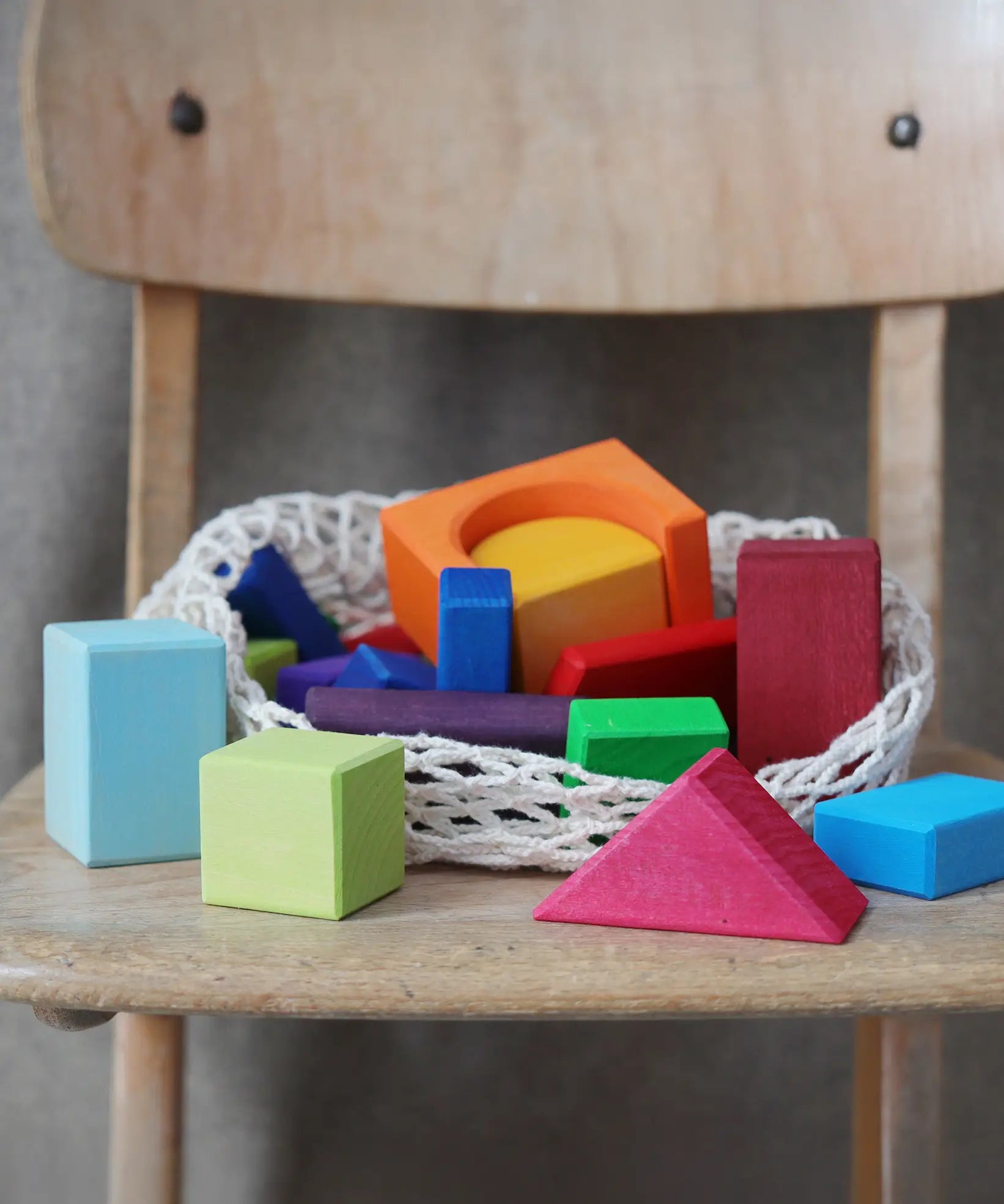Grimm's 30 Coloured wooden Geo Blocks placed on a wooden chair.