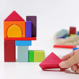Grimm's 30 Coloured wooden Geo Blocks, an adult's hand can be seen holding one of the triangle shaped pieces.