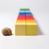 Grimm's 36 rainbow cubes wooden blocks lined up next to a snail shell.
