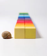 Grimm's 36 rainbow cubes wooden blocks lined up next to a snail shell.