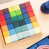 Grimm's 36 rainbow cubes wooden blocks in a storage tray next to a polar light set and purple wooden pebbles