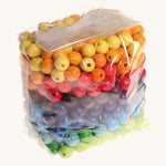 Rainbow coloured wooden Grimms beads in bag on a cream background.