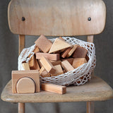 Grimm's 60 natural geo wooden building blocks in a net storage bag placed on a wooden chair.