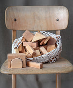 Grimm's 60 natural geo wooden building blocks in a net storage bag placed on a wooden chair.