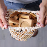 Grimm's 60 natural geo wooden building blocks in a net storage bag held in an adult's hands. 