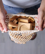 Grimm's 60 natural geo wooden building blocks in a net storage bag held in an adult's hands. 