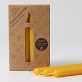 A pack of 12 Grimm's amber 100% beeswax candles in a cardboard box with three candles at the front laid out in front of the box.