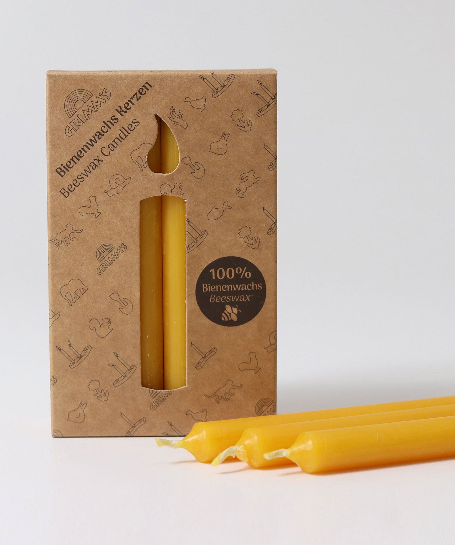 A pack of 12 Grimm's amber 100% beeswax candles in a cardboard box with three candles at the front laid out in front of the box.