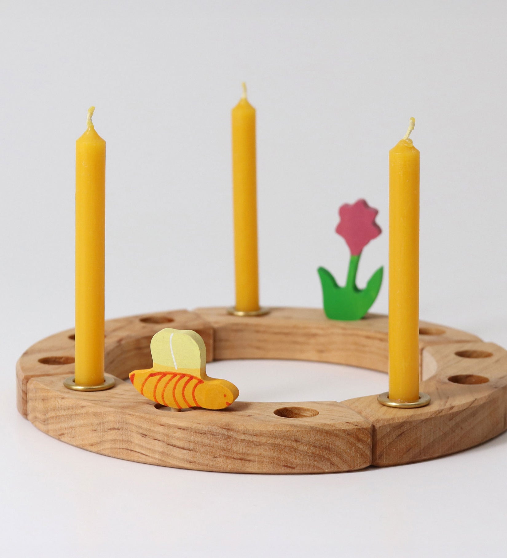 Grimm's Amber beeswax candles placed on a natural celebration ring with a pink flower and bee wooden decorative figures.