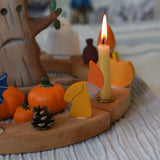 A Grimm's Autumn dwarf decorative figure placed on a natural celebration ring.  A lit beeswax candle and other Autumnal themed decorative items have also been placed on the ring. 