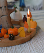 A Grimm's Autumn dwarf decorative figure placed on a natural celebration ring.  A lit beeswax candle and other Autumnal themed decorative items have also been placed on the ring. 