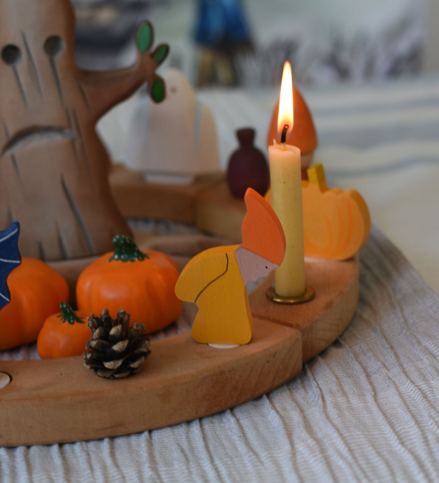 A Grimm's Autumn dwarf decorative figure placed on a natural celebration ring.  A lit beeswax candle and other Autumnal themed decorative items have also been placed on the ring. 
