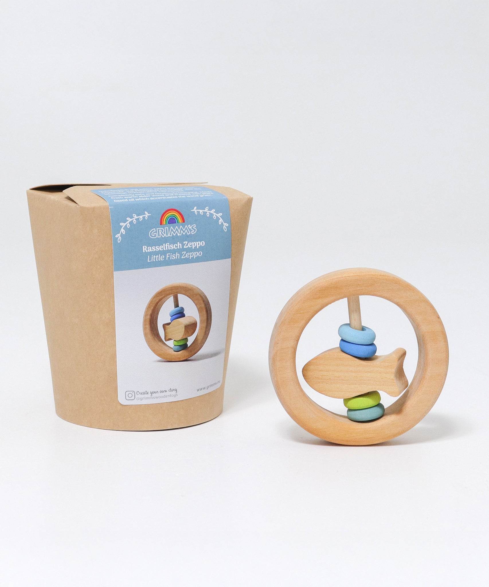 The Grimm's baby Grasping Toy Little Fish With Wooden Discs pictured next to it's plastic free cardboard packaging box.