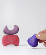 Piece of the Grimm's purple bakery block house wooden toy shown in an adult's fingers.