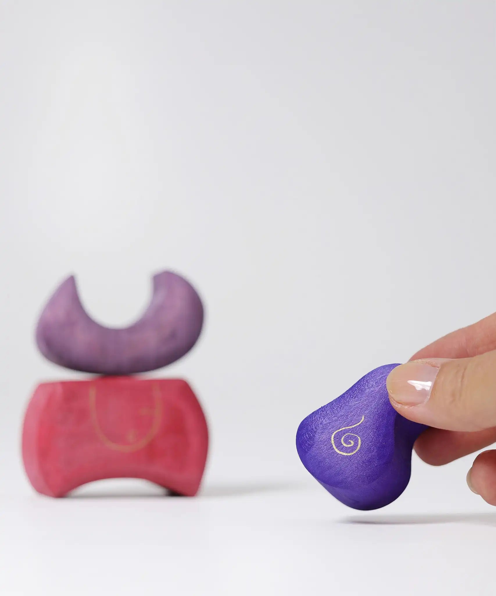 Piece of the Grimm's purple bakery block house wooden toy shown in an adult's fingers.