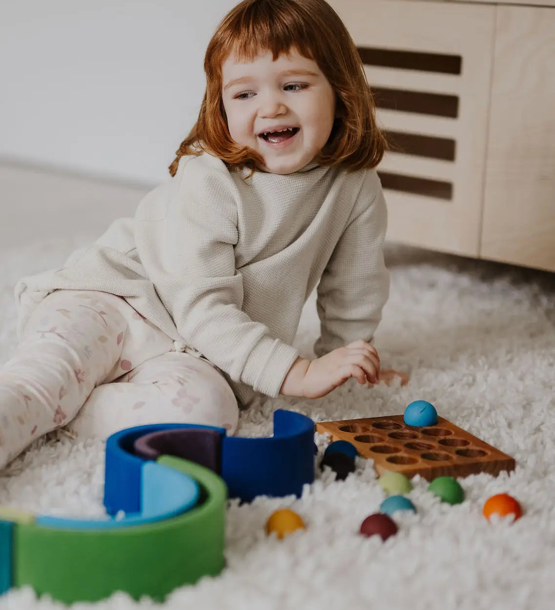 Child next to a ball run and sorting board with the Grimms small wooden rainbow balls