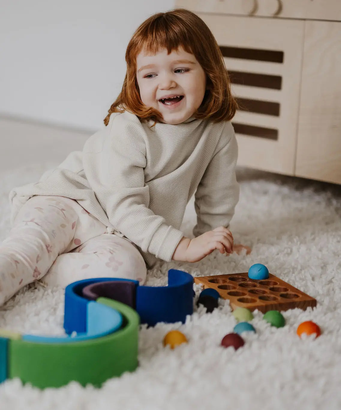 Child next to a ball run and sorting board with the Grimms small wooden rainbow balls