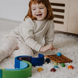 Child next to a ball run and sorting board with the Grimms small wooden rainbow balls