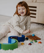 Child next to a ball run and sorting board with the Grimms small wooden rainbow balls