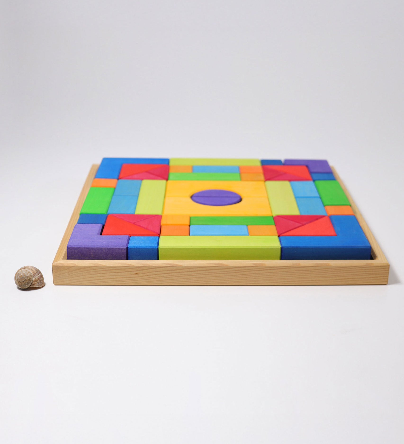 The Grimm's Basic Building Set 2 wooden block set shown in it's wooden storage tray next to a snail's shell. 