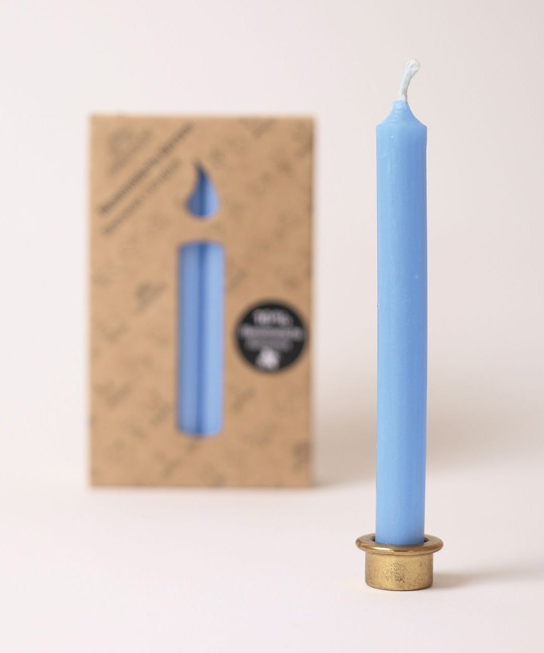 A blue Grimm's beeswax candle in a metal stand, with a packet of candles in the background. 