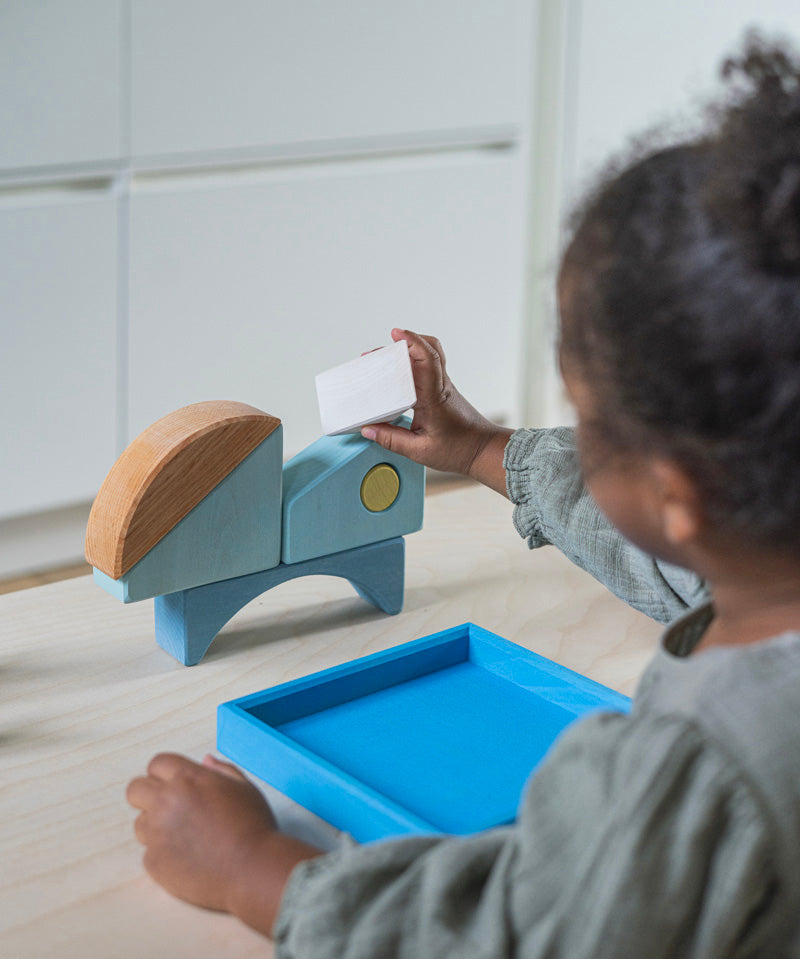 A child playing with the Grimm's blue boat Wooden Stacking Puzzle. The child is stacking the blocks on top of each other. These Grimm's toys are part of a wide range of wooden toys available here at Babipur. 
