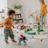 Child playing the Grimms handcrafted wooden blue elephant in a playroom with a waldorf doll sitting on top 
