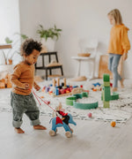 Child playing the Grimms handcrafted wooden blue elephant in a playroom with a waldorf doll sitting on top 