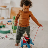 Child pulling the Grimms handcrafted wooden blue elephant in a playroom with a waldorf doll sitting on top 