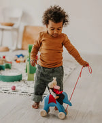 Child pulling the Grimms handcrafted wooden blue elephant in a playroom with a waldorf doll sitting on top 