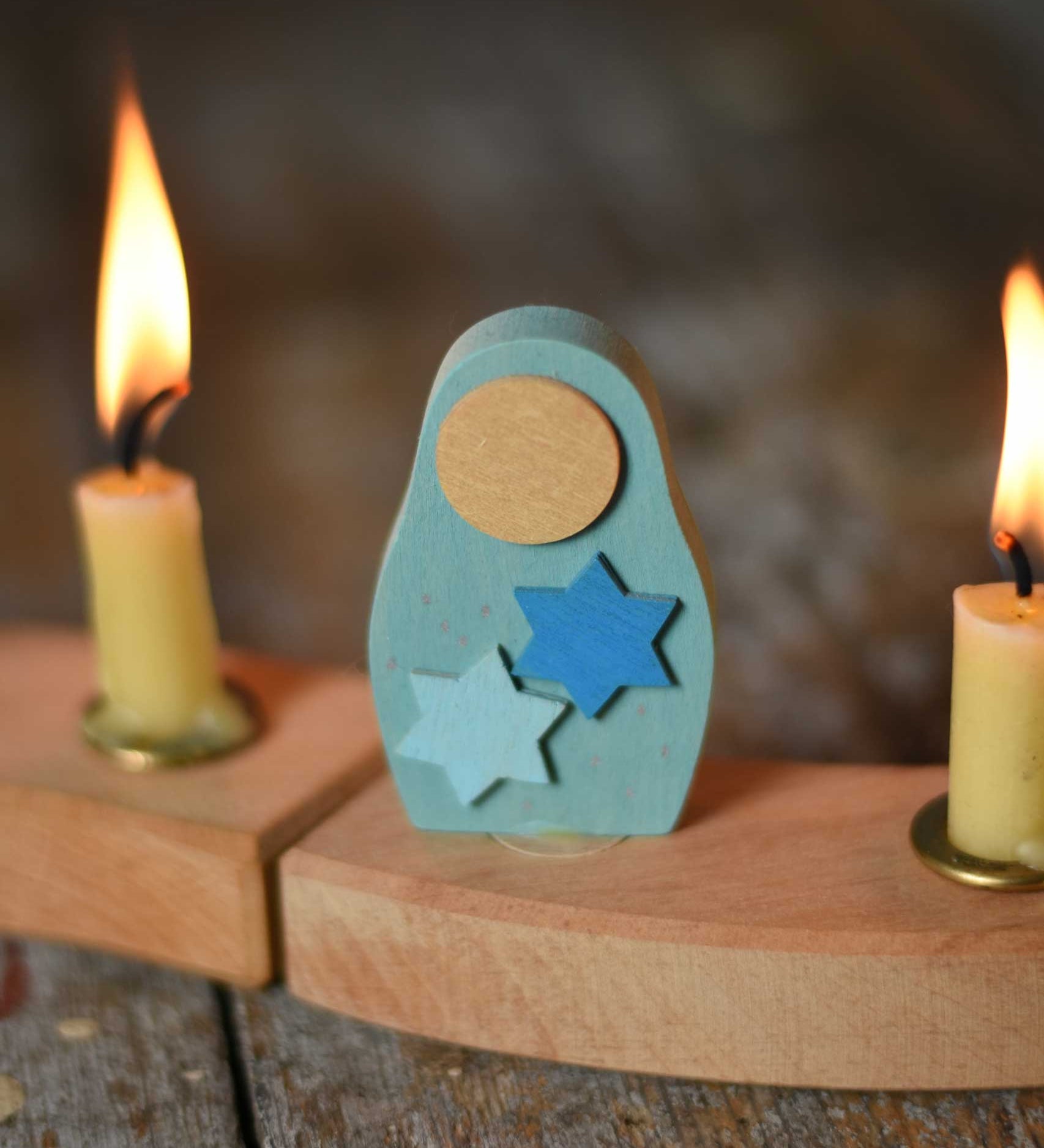 A Grimm's Matryoshka Stars Decorative Figure placed in between two lit candles on a natural celebration ring. 