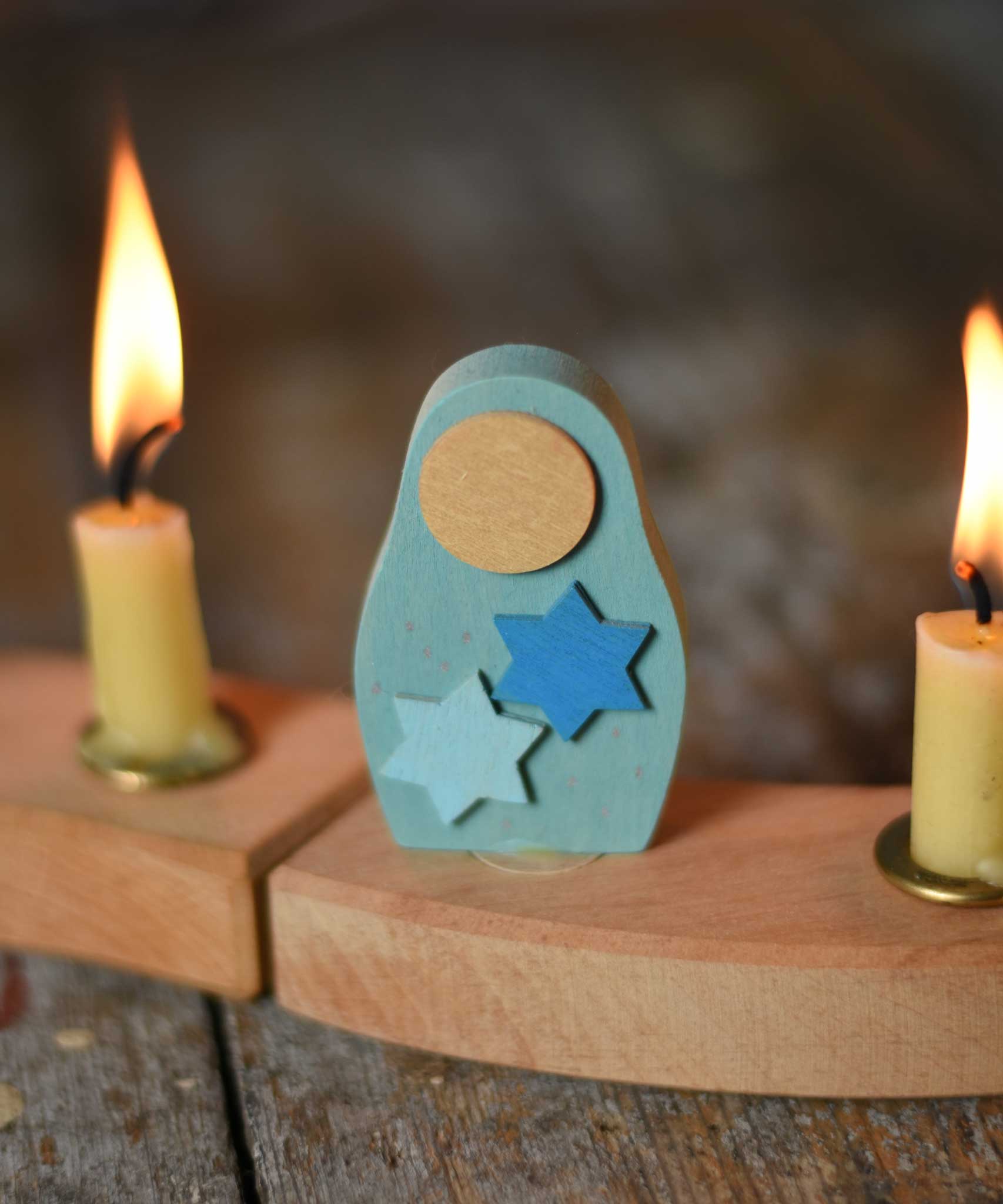 A Grimm's Matryoshka Stars Decorative Figure placed in between two lit candles on a natural celebration ring. 