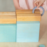 Child rolling a ring down a wooden rail on top of the Grimms large pastel building boxes