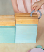 Child rolling a ring down a wooden rail on top of the Grimms large pastel building boxes