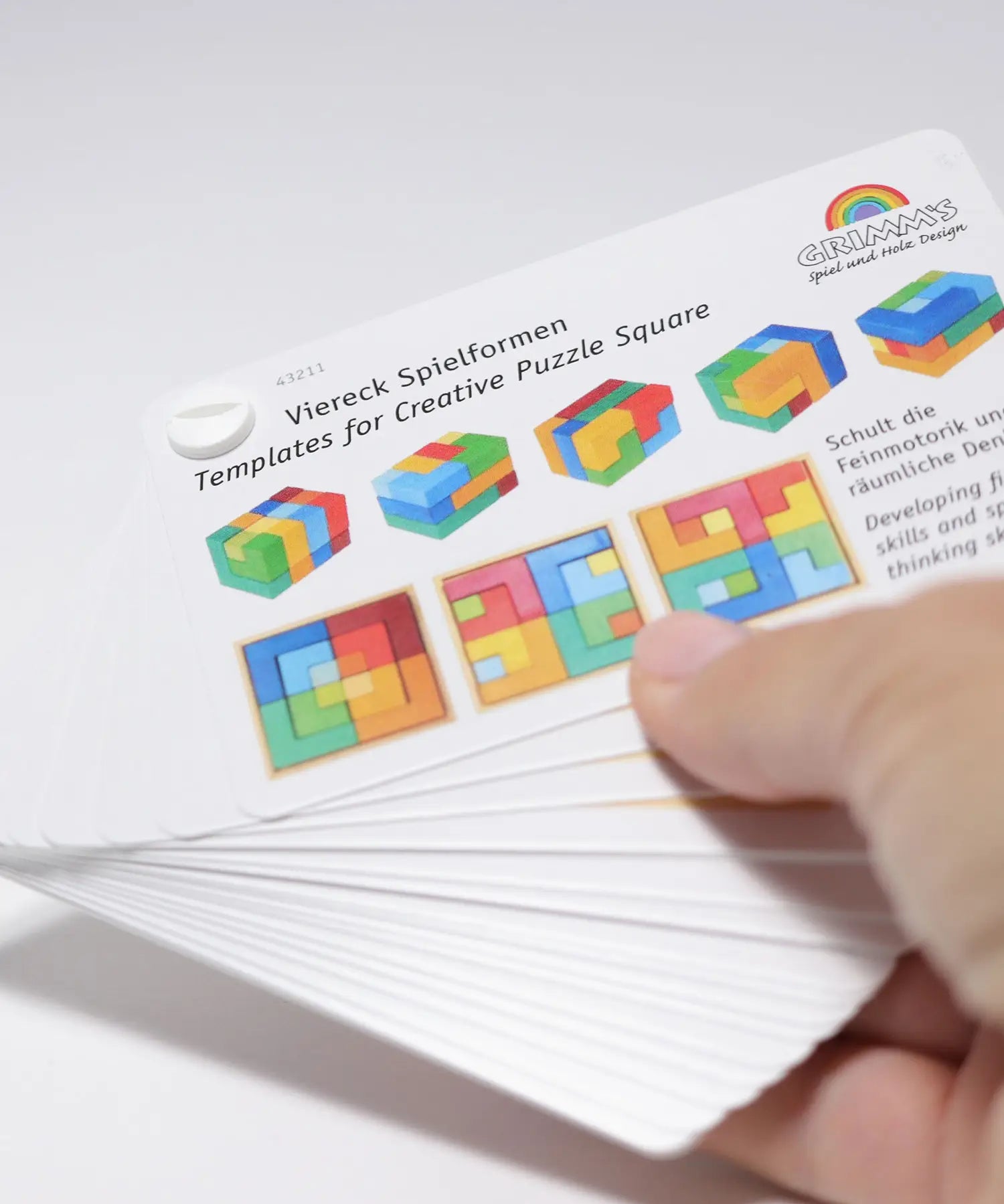 Adult hand holding the Grimm's puzzle square booklet showing scale