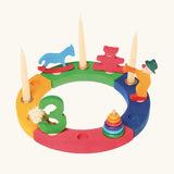 Grimms bright wooden celebration ring pieces displaying decorative figures including a rocking horse, teddy bear, clown conical tower and a number 3 figure