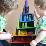 Children sitting next o a stack made from Grimms bright rainbow building blocks including semi circles and arch pieces