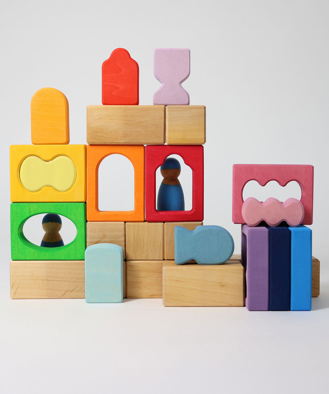 The blocks from the Grimm's Windows Building Set wooden blocks placed in a stack on top of each other. Grimm's friends peg dolls can be seen behind them. These Grimm's wooden blocks are part of a wide range of wooden toys available here at Babipur. 