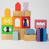 The blocks from the Grimm's Windows Building Set wooden blocks placed in a stack on top of each other. Grimm's friends peg dolls can be seen behind them. These Grimm's wooden blocks are part of a wide range of wooden toys available here at Babipur. 