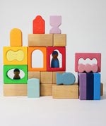 The blocks from the Grimm's Windows Building Set wooden blocks placed in a stack on top of each other. Grimm's friends peg dolls can be seen behind them. These Grimm's wooden blocks are part of a wide range of wooden toys available here at Babipur. 