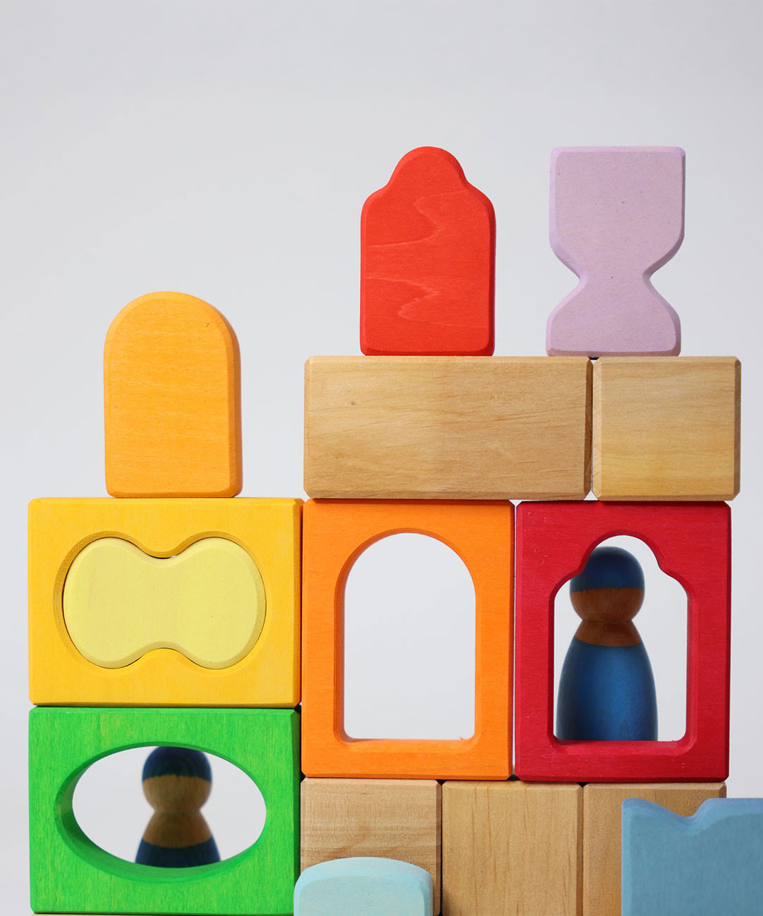 The blocks from the Grimm's Windows Building Set wooden blocks placed in a stack on top of each other. Grimm's friends peg dolls can be seen behind them. These Grimm's wooden blocks are part of a wide range of wooden toys available here at Babipur. 