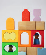 The blocks from the Grimm's Windows Building Set wooden blocks placed in a stack on top of each other. Grimm's friends peg dolls can be seen behind them. These Grimm's wooden blocks are part of a wide range of wooden toys available here at Babipur. 