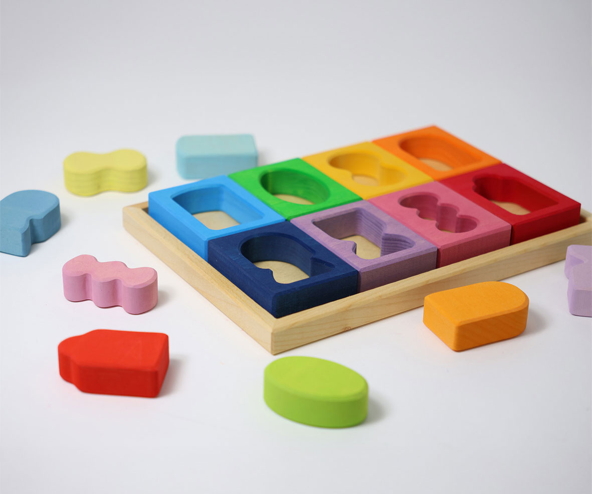 Grimm's Windows Building Set wooden blocks in a wooden storage tray. The shaped inserts from the window blocks have been taken out and placed around the tray. These Grimm's wooden blocks are part of a wide range of wooden toys available here at Babipur. 