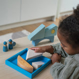 A child playing with the Grimm's blue boat Wooden Stacking Puzzle. The child is placing the blocks into the blue coloured wooden tray. These Grimm's toys are part of a wide range of wooden toys available here at Babipur. 